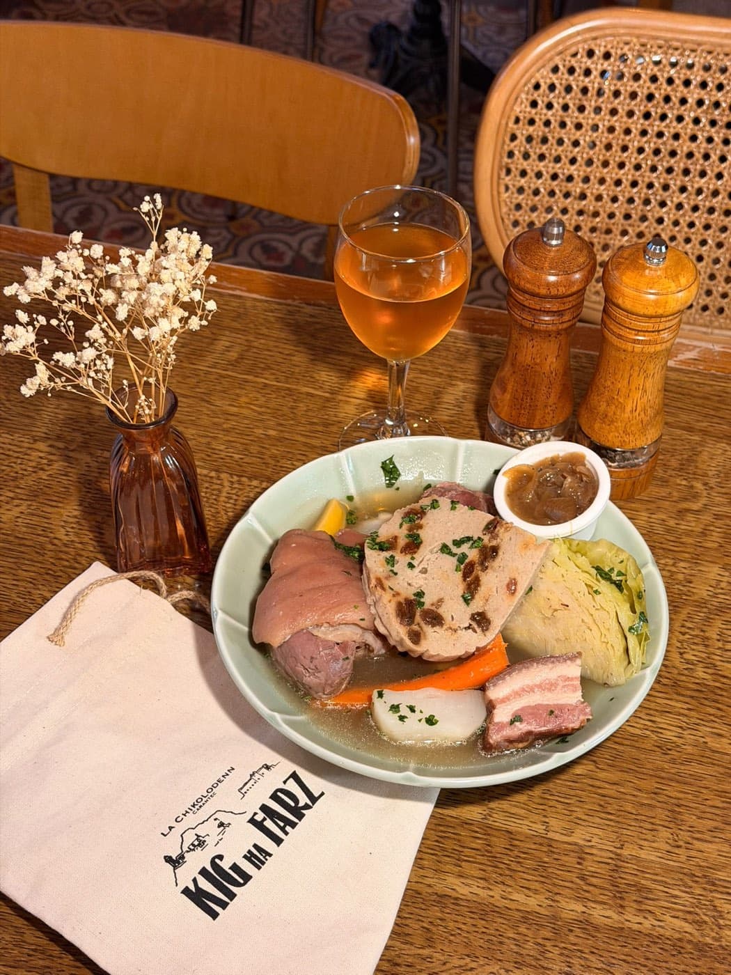 Kig ha farz servi sur une table en bois chez Ty Louis : la tranche de farz de blé noir aux raisins posée sur les viandes et les légumes du bouillon, la sauce lipig à part