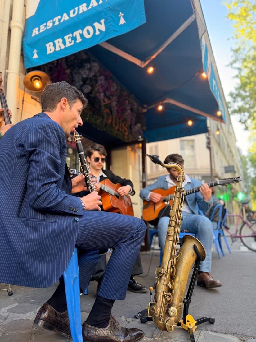Un saxophoniste et des guitaristes jouent en terrasse de Ty Louis sous l’auvent « Restaurant breton », à la lumière du soir
