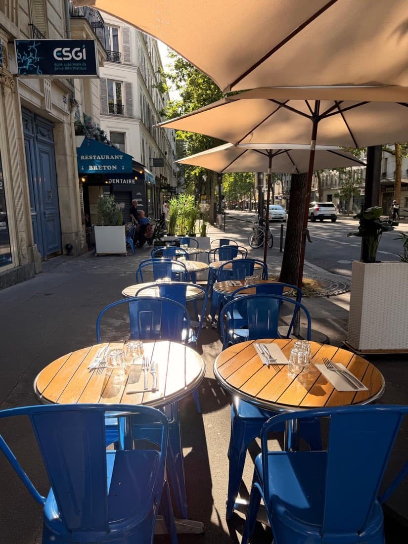 Tables en bois et chaises bleues dressées sur la terrasse de Ty Louis à la lumière dorée du soir